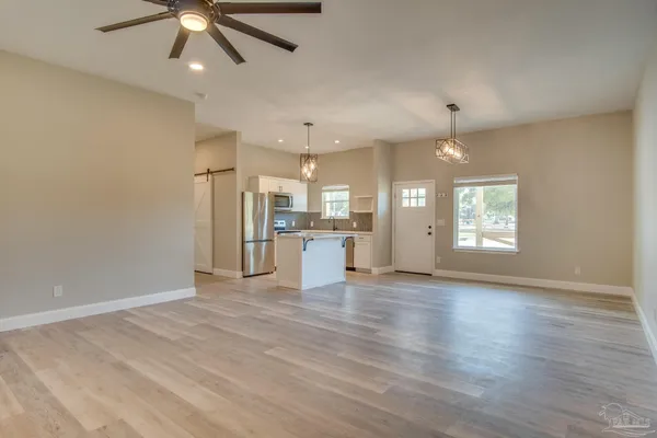an empty room with wooden floor a ceiling fan and kitchen view