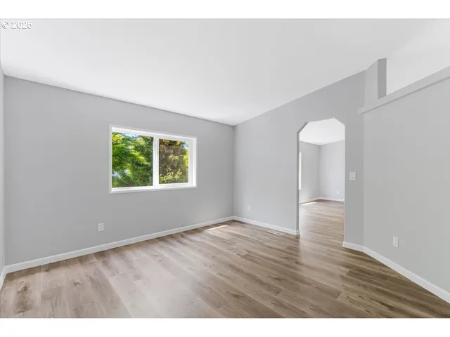 a view of an empty room with wooden floor and window