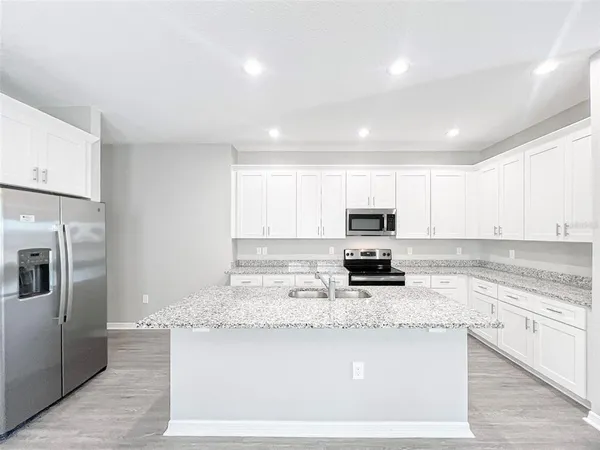 a kitchen with granite countertop a stove top oven a sink a refrigerator and white cabinets