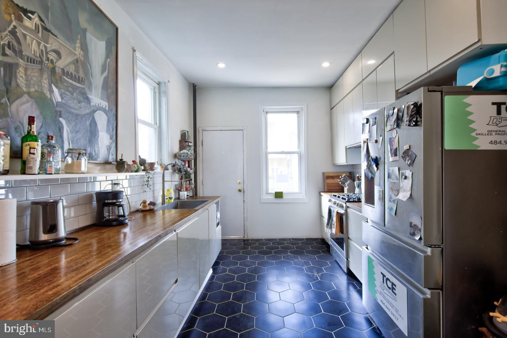 2044 Tasker Street Philadelphia, PA 19145 - Photo 5 of 15 a kitchen with stainless steel appliances a refrigerator a stove a sink and white cabinets with wooden floor