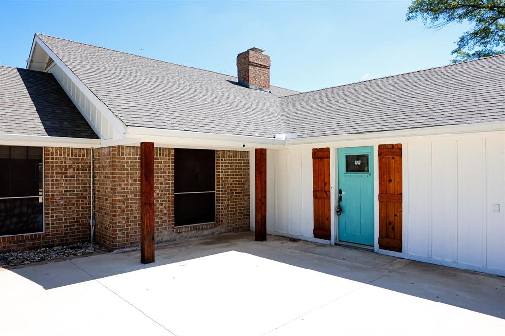 10575 Friendship Road Pilot Point, TX 76258 - Photo 17 of 32 Exterior entry featuring a vibrant turquoise door, decorative wooden shutters, brick facade, white board and batten siding, and a gabled roofline
