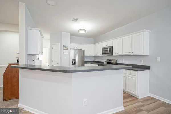 a kitchen with stainless steel appliances granite countertop a sink a stove a refrigerator with white cabinets and wooden floor