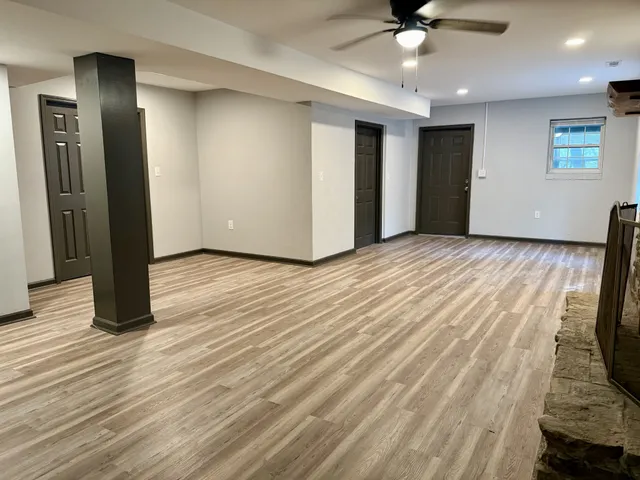 a view of an empty room with wooden floor and a ceiling fan