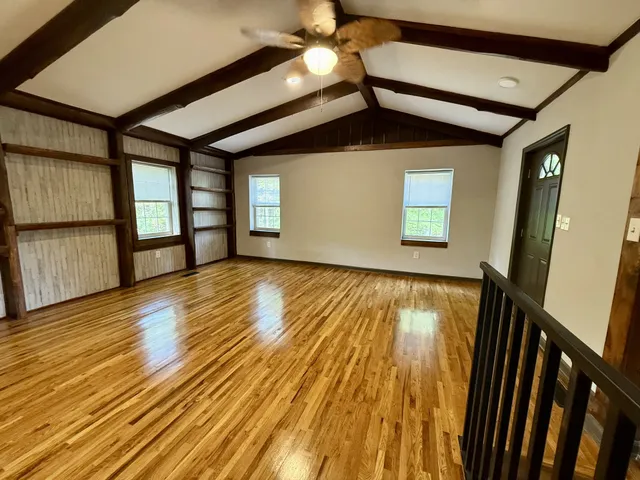 a view of an empty room with wooden floor and fan