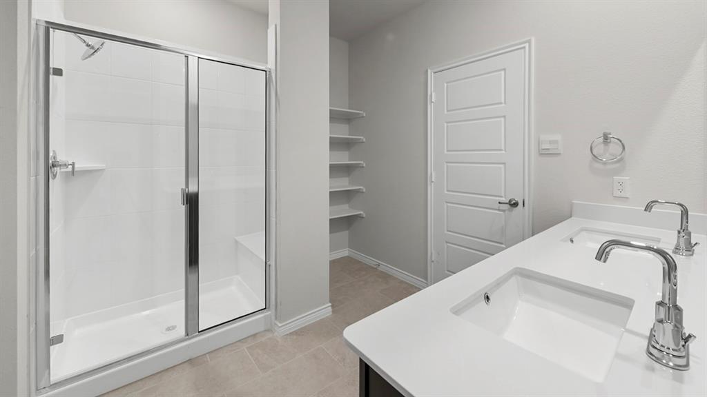 412 Carthage Street Caddo Mills, TX 75135 - Photo 4 of 32 Bathroom featuring a dual vanity with white countertops and chrome fixtures, a glass-enclosed shower with white subway tile, and recessed shelving