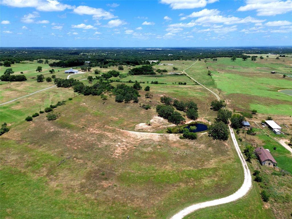 2186 Gilliland Road Springtown, TX 76082 - Photo 22 of 25 Expansive rural landscape featuring a winding dirt road, scattered trees, and a visible pond