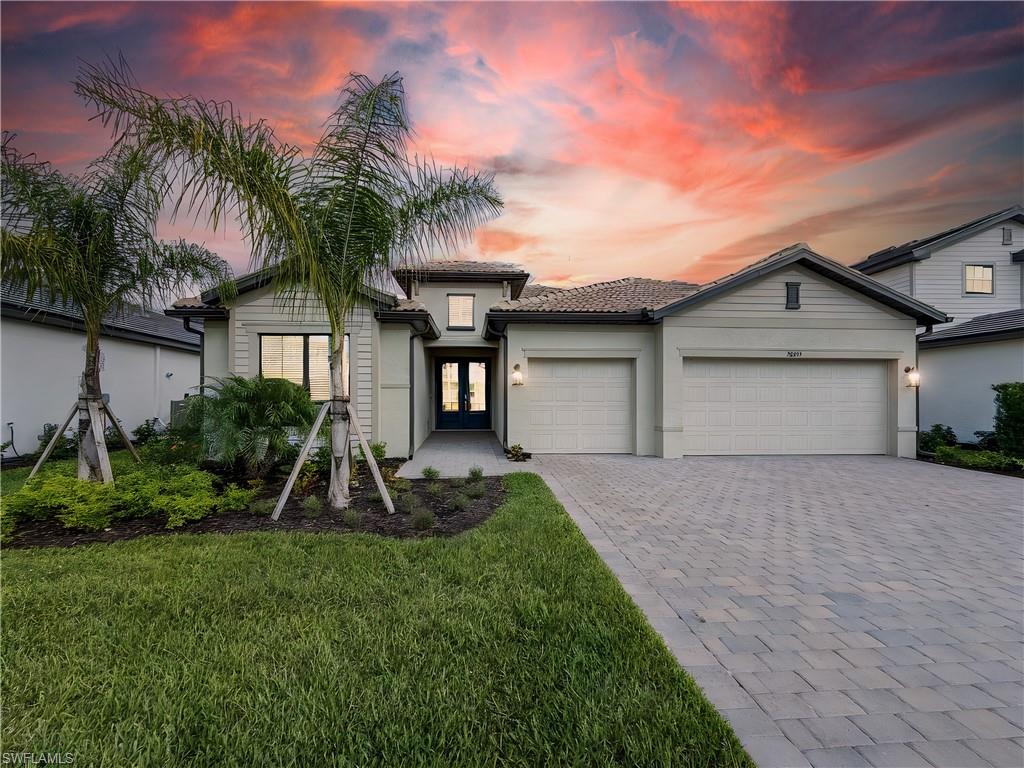 View of front of home with decorative driveway, a garage, a front yard, stucco siding, and a tiled roof