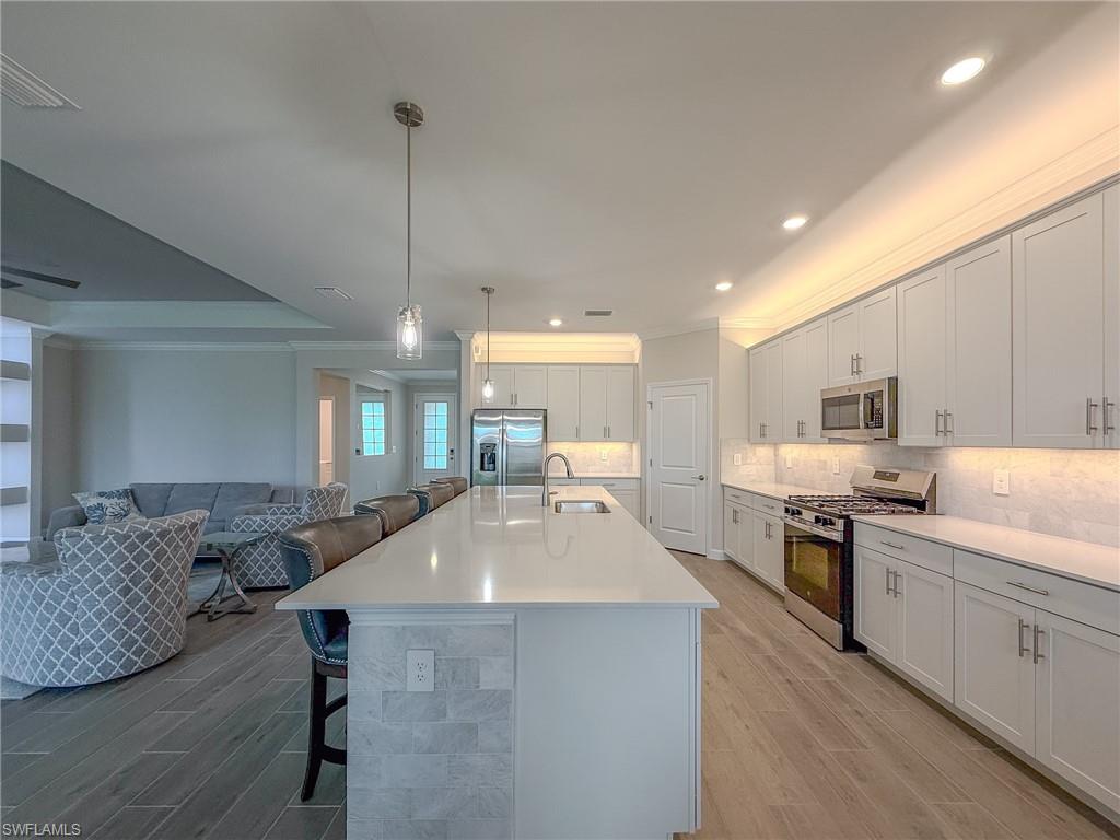 20489 Verawood Loop Estero, FL 33928 - Photo 12 of 50 Kitchen with crown molding, appliances with stainless steel finishes, a kitchen breakfast bar, wood finish floors, and pendant lighting