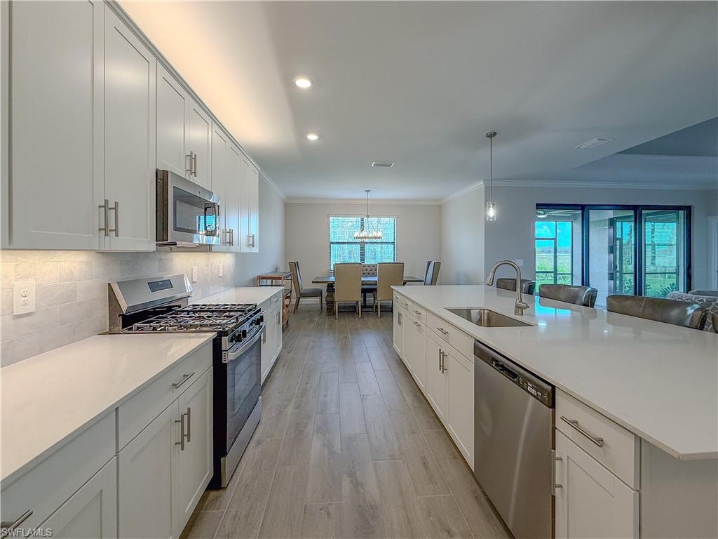 20489 Verawood Loop Estero, FL 33928 - Photo 13 of 50 Kitchen featuring appliances with stainless steel finishes, crown molding, light stone counters, white cabinetry, and decorative light fixtures