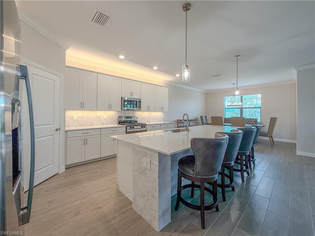 20489 Verawood Loop Estero, FL 33928 - Photo 9 of 50 Kitchen featuring decorative light fixtures, crown molding, stainless steel appliances, wood tiled floors, and an island with sink