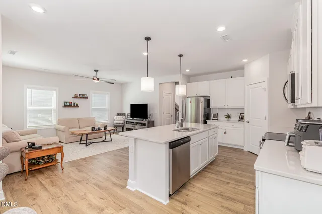 a large white kitchen with a stove a sink a kitchen island with furniture and wooden floor