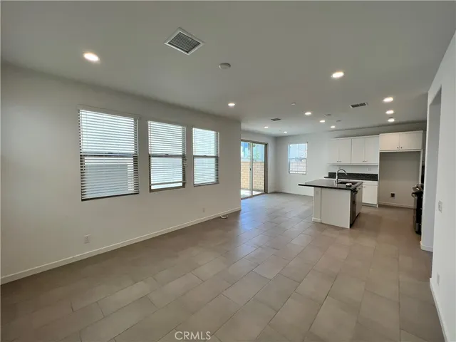 a view of an empty room with a window and kitchen view