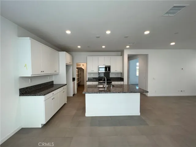 a large white kitchen with stainless steel appliances kitchen island a stove a refrigerator a oven a dining table and chairs