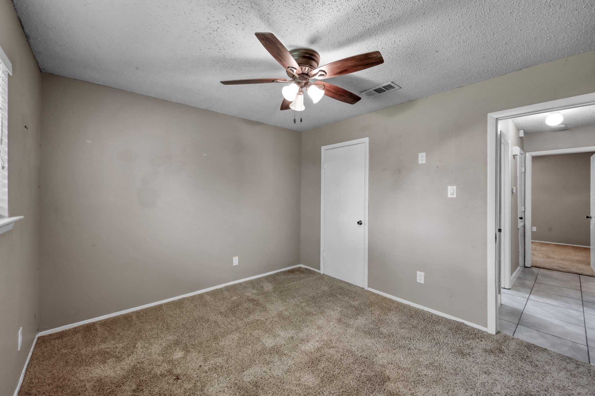 12015 Fallbrook Drive Houston, TX 77065 - Photo 24 of 29 This room features neutral walls, a carpeted floor, and a ceiling fan with lights. It has a window for natural light and leads to adjacent rooms with tiled flooring.