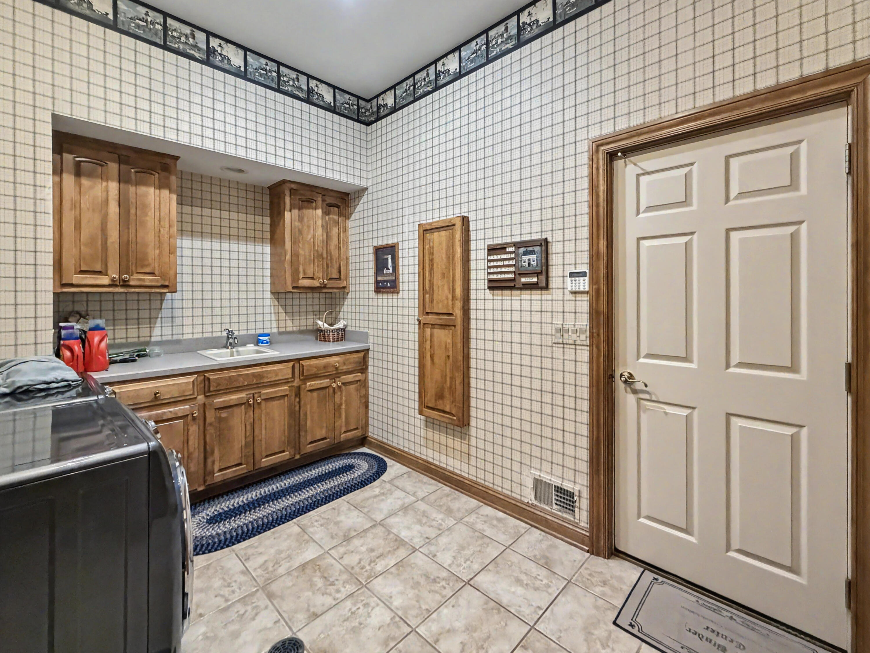W291-s5245 Ridgefield Road Waukesha, WI 53189 - Photo 38 of 44 Convenient & Spacious mudroom and laundry center off the garage offers custom birch cabinetry, generous workspace, utility sink, tile flooring, floor drain, and ample storage