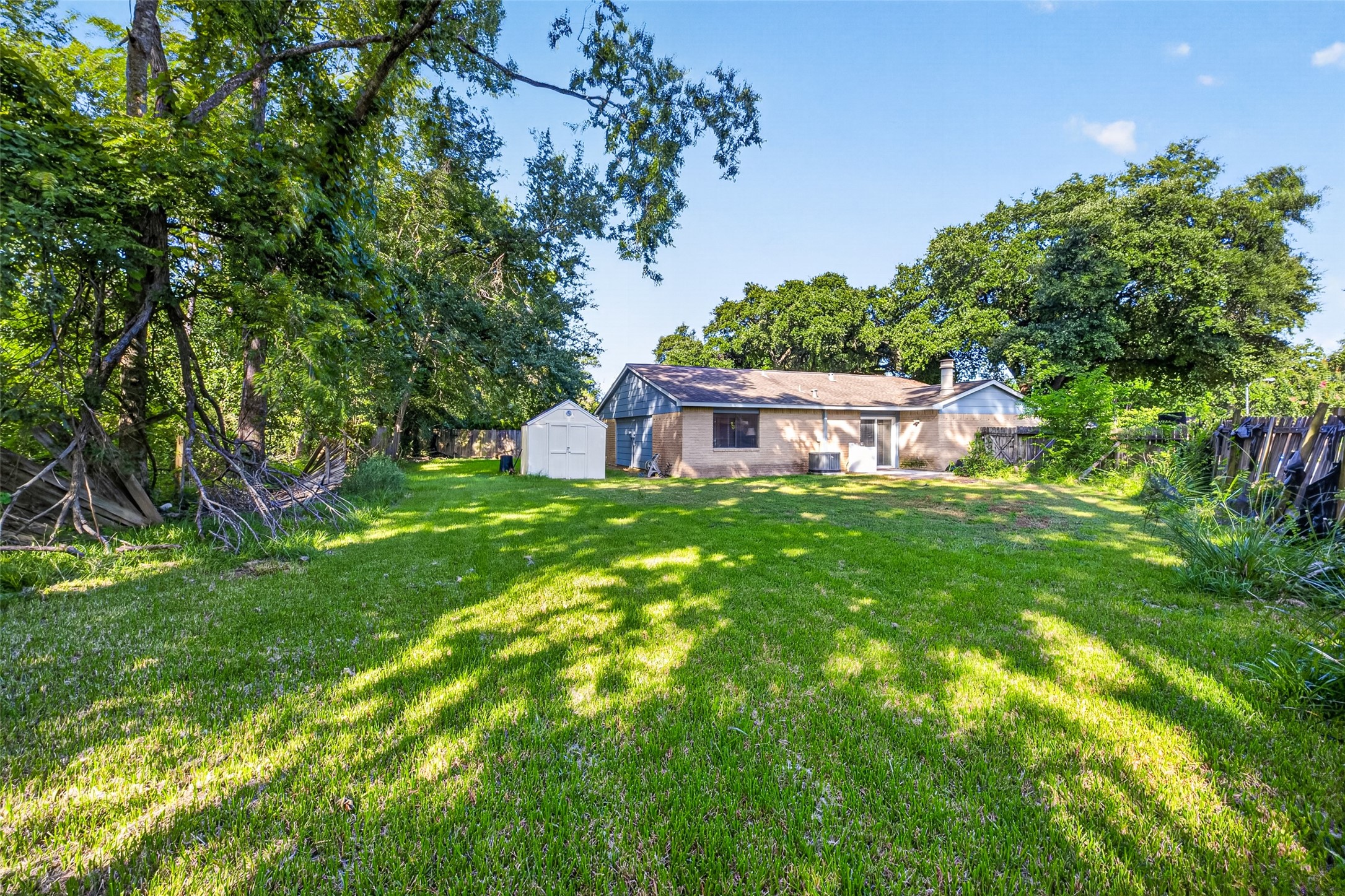 22926 Millgate Drive Spring, TX 77373 - Photo 29 of 34 Spacious backyard with lush grass and mature trees, featuring a small shed and a single-story house with a light brick exterior. Ideal for outdoor activities and relaxation.