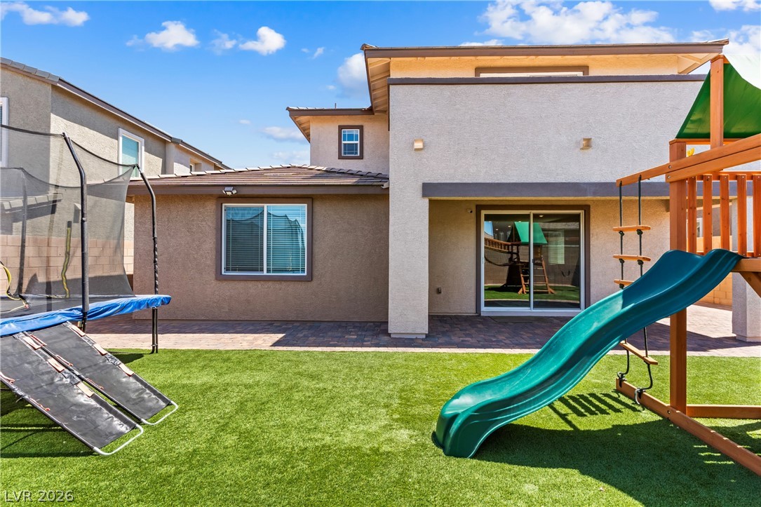 320 Isla Enclave Way Henderson, NV 89011 - Photo 37 of 49 The private yard features an artificial turf lawn, a children's play set, and a trampoline, all enclosed by the home's exterior.