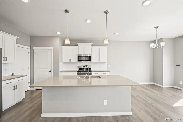 a large kitchen with granite countertop a stove a sink and white cabinets with wooden floor