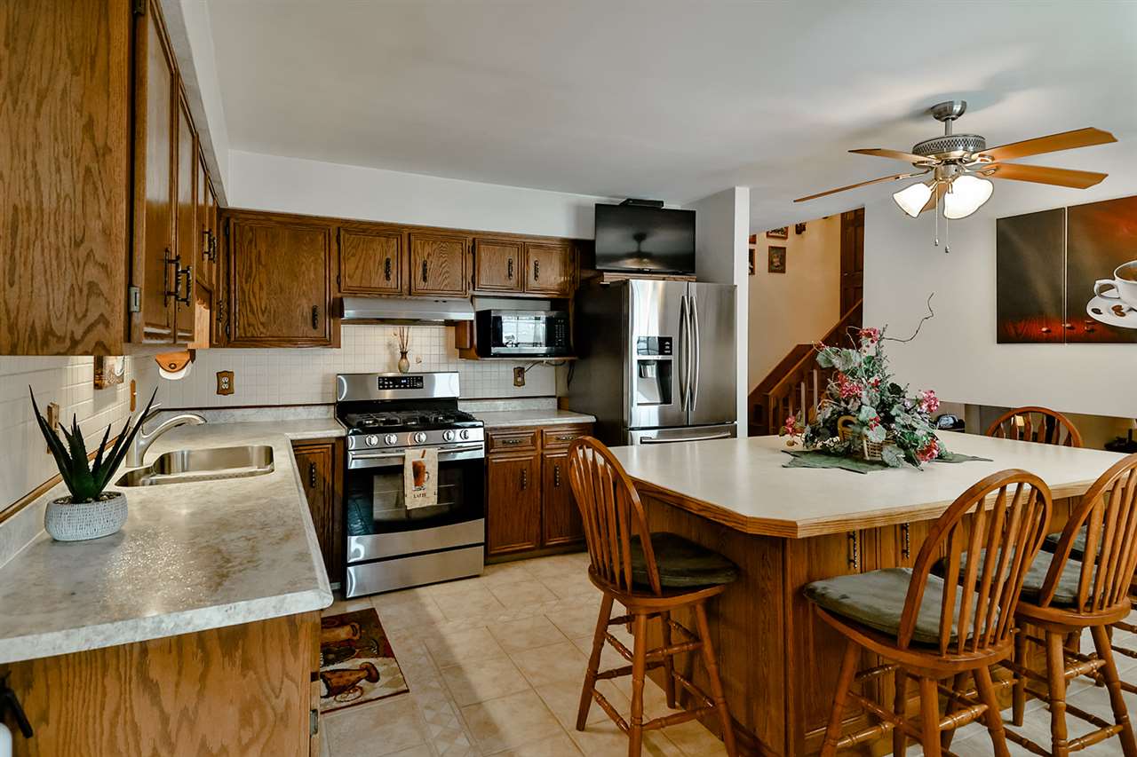 12944 Huntsboro Lane Roscoe, IL 61073 - Photo 11 of 40 a kitchen with stainless steel appliances granite countertop a stove a refrigerator a sink a dining table and chairs with wooden floor