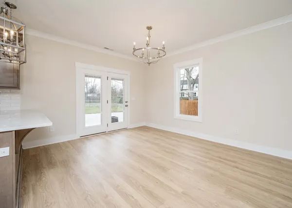 an empty room with wooden floor chandelier and windows