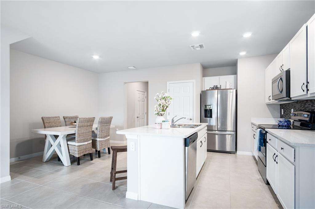 15070 Wildflower Circle Naples, FL 34119 - Photo 7 of 22 a kitchen with stainless steel appliances a refrigerator a stove a sink dishwasher and white cabinets with wooden floor
