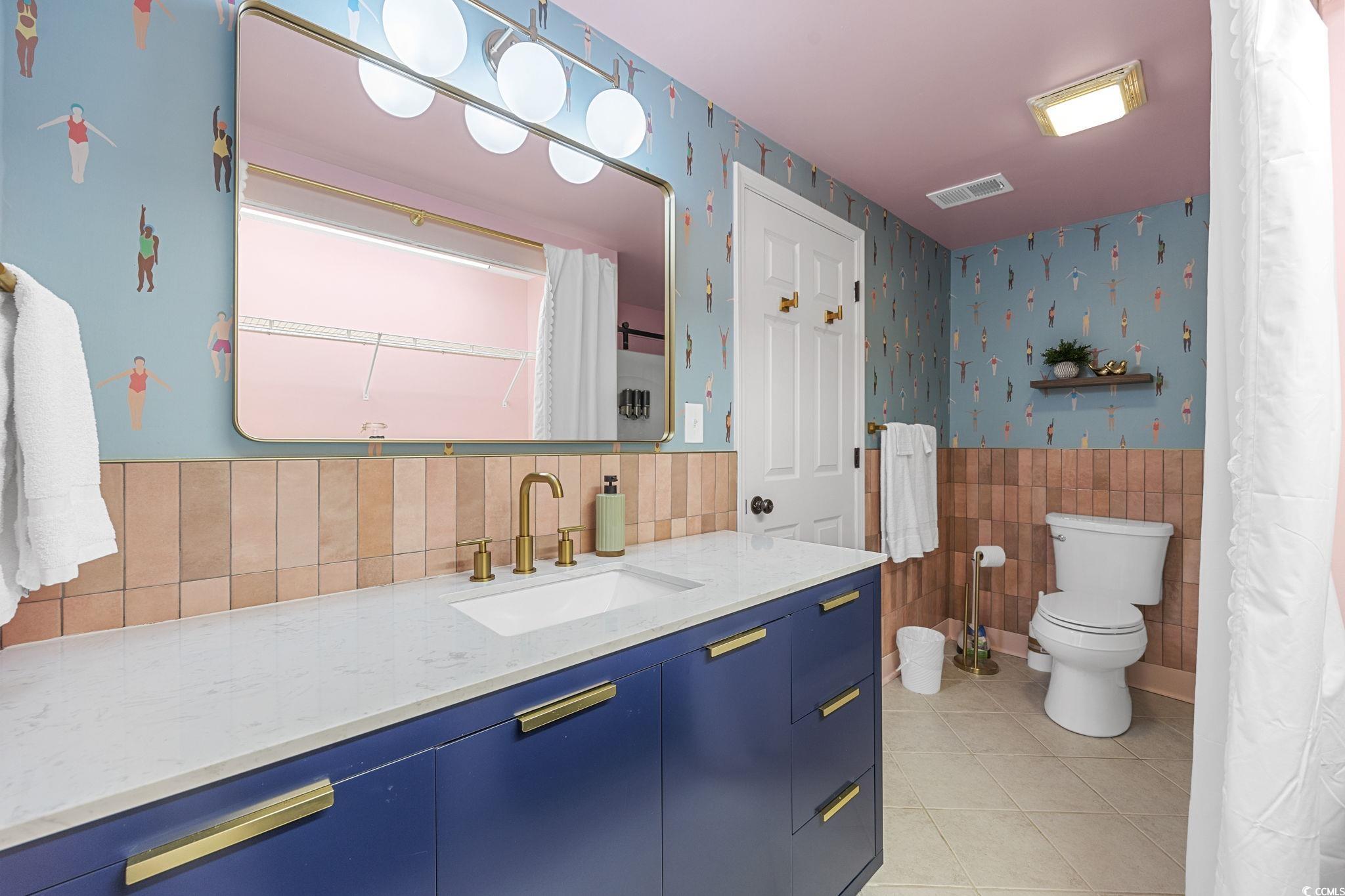 104 Ash Street North Myrtle Beach, SC 29582 - Photo 21 of 39 Bathroom featuring light tile patterned floors, vanity, wallpapered walls, a wainscoted wall, and tile walls