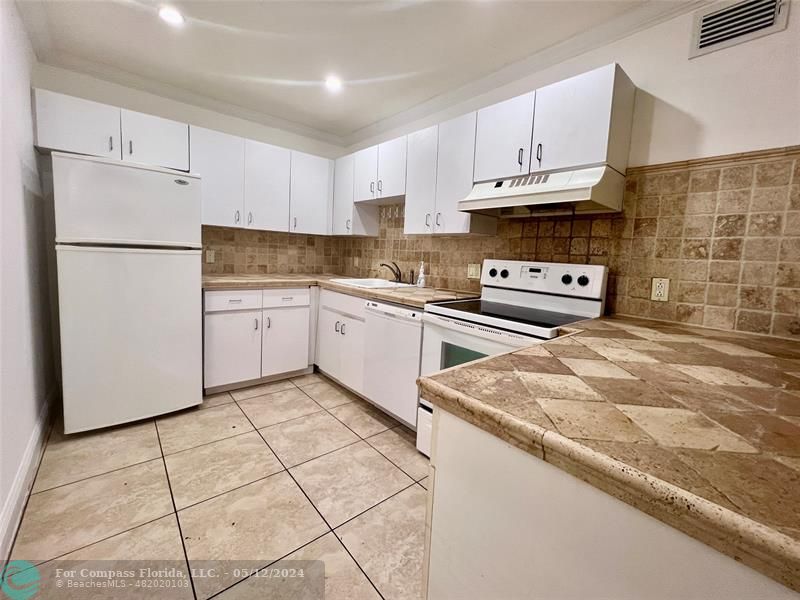 a kitchen with stainless steel appliances granite countertop a refrigerator sink stove and white cabinets