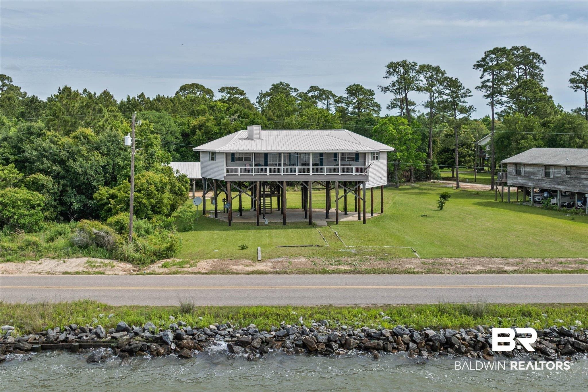 9100 Shell Belt Road Coden, AL 36523 - Photo 1 of 38 Stilted coastal home featuring a metal roof and a spacious screened-in porch with white railings