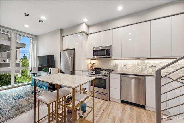 a kitchen with stainless steel appliances granite countertop a stove top oven a sink dishwasher a refrigerator and white cabinets with wooden floor