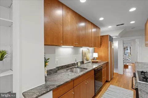 a kitchen with granite countertop stainless steel appliances a sink a counter top space cabinets and wooden floor