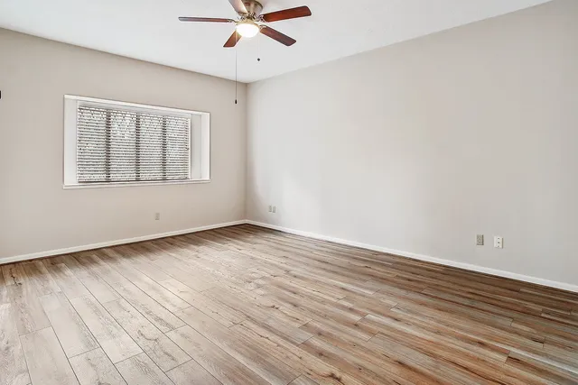 an empty room with wooden floor fan and windows