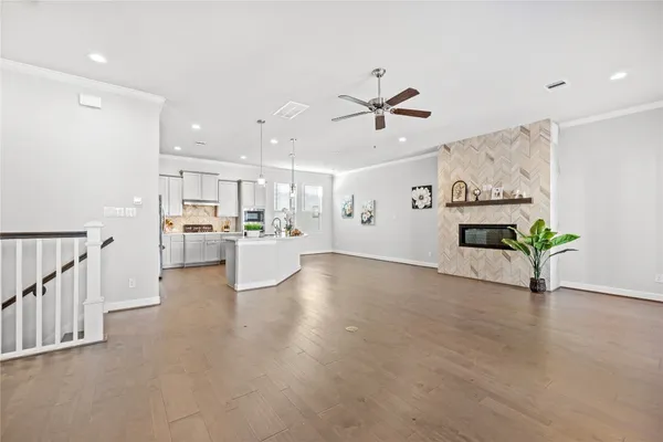 a view of an empty room and kitchen with furniture a ceiling fan and wooden floor