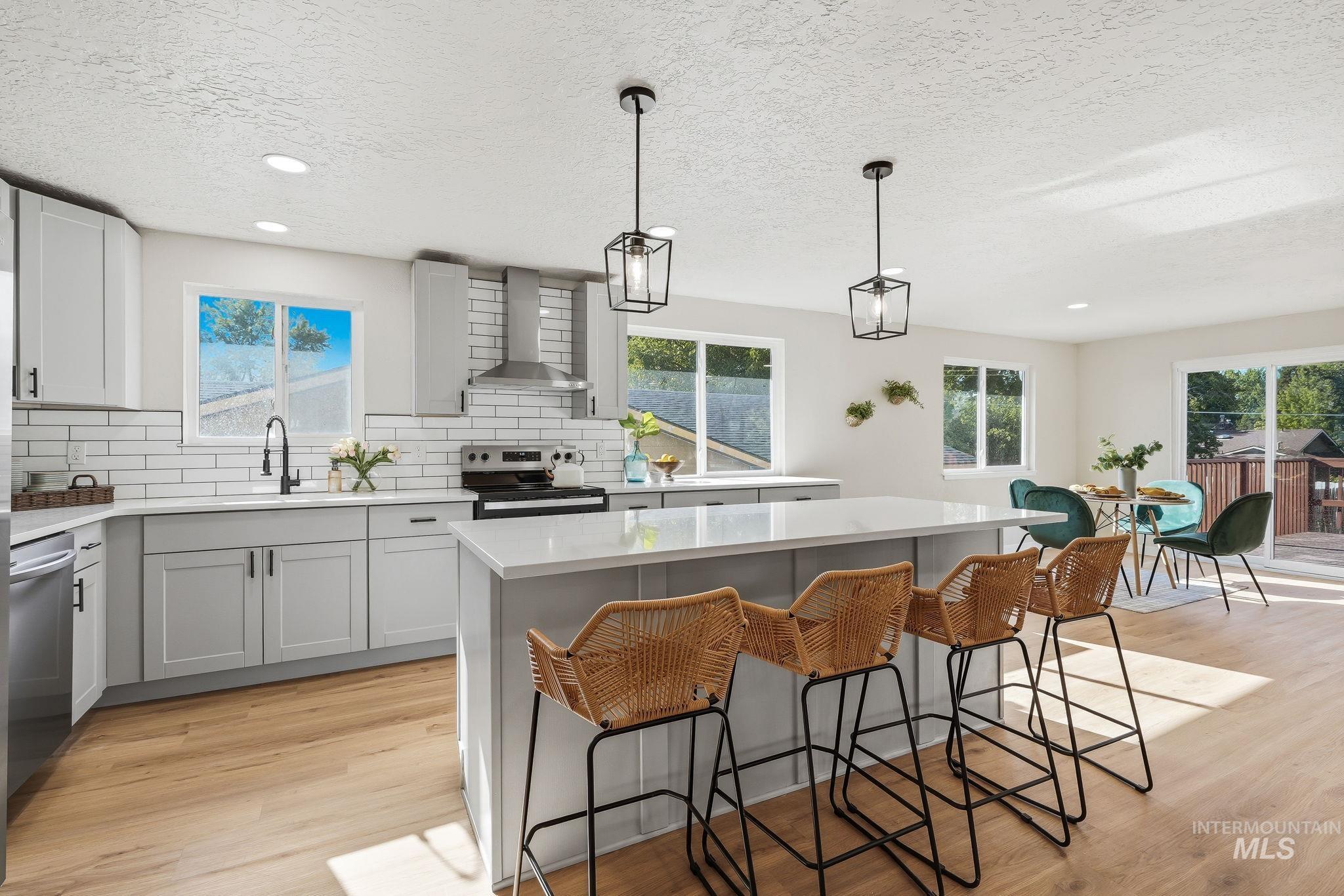1990 Panama Street Boise, ID 83705 - Photo 20 of 50 Contemporary kitchen featuring an expansive island with a light-toned countertop, a range with stainless steel hood, white subway tile backsplash, and light wood-finish flooring
