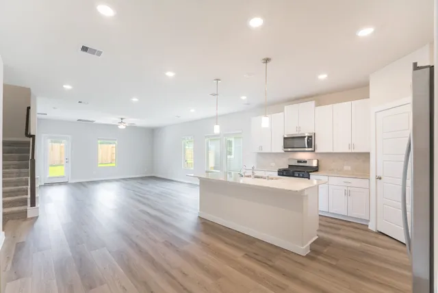 a large kitchen with stainless steel appliances refrigerator a stove top oven a sink dishwasher and white cabinets with wooden floor