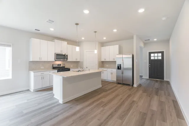 a large kitchen with stainless steel appliances granite countertop a stove a sink a refrigerator white cabinets and wooden floor