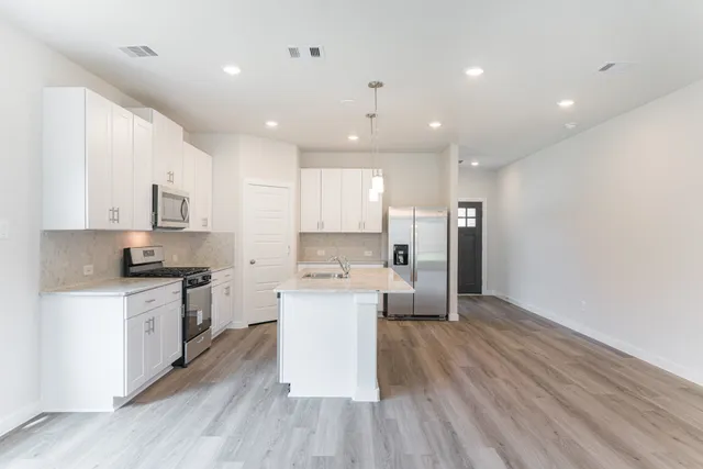a large kitchen with a large counter top a sink stainless steel appliances and cabinets