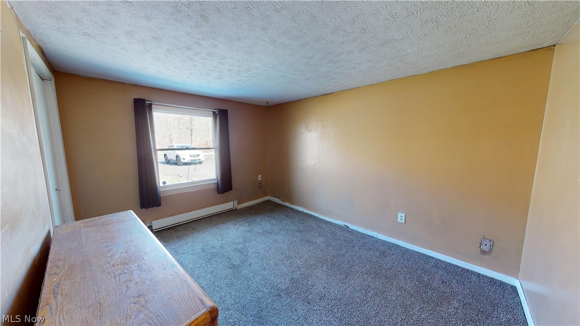 6970 Bushnell Road Conneaut, OH 44030 - Photo 3 of 28 Carpeted spare room with a textured ceiling and a baseboard heating unit