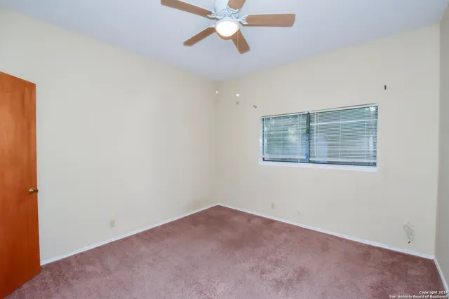 an empty room with chandelier fan and windows