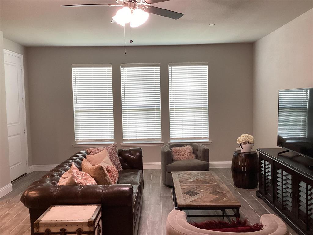 5984 Bursey Road Watauga, TX 76148 - Photo 5 of 21 Living area featuring three large windows with blinds, wood-finish flooring, and a ceiling fan with integrated lighting