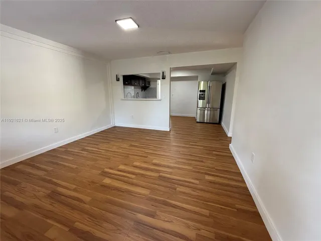 a view of a hallway with wooden floor and a refrigerator