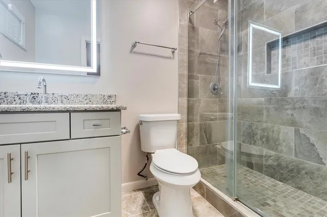 a bathroom with a granite countertop toilet a sink a mirror and shower