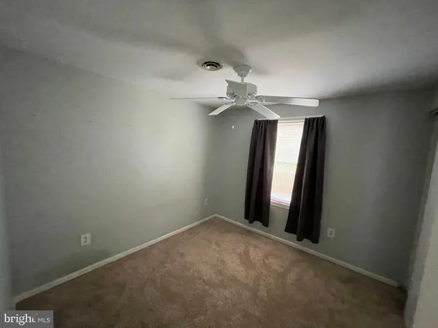 an empty room with a chandelier fan and wooden floor