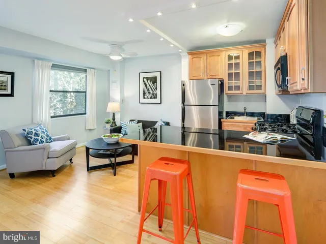 a kitchen with stainless steel appliances granite countertop a refrigerator a sink dishwasher a dining table and with couches next to a window