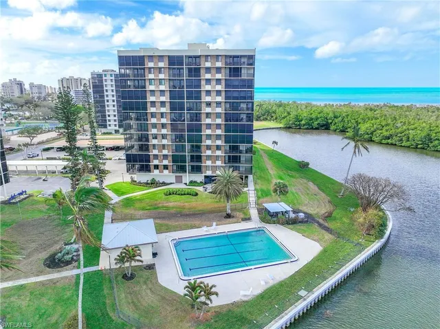 a view of a swimming pool with lawn chairs plants and large trees