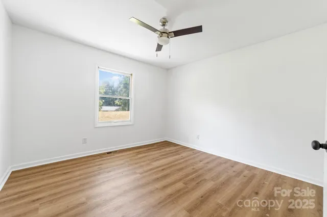 an empty room with wooden floor ceiling fan and windows