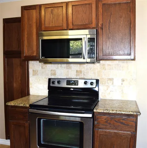 a stove top oven sitting inside of a kitchen with granite countertop wooden cabinets