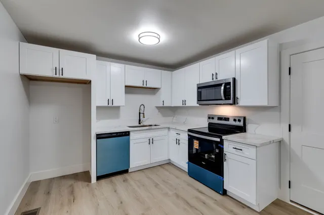 a kitchen with stainless steel appliances granite countertop white cabinets a sink a stove a microwave and a refrigerator