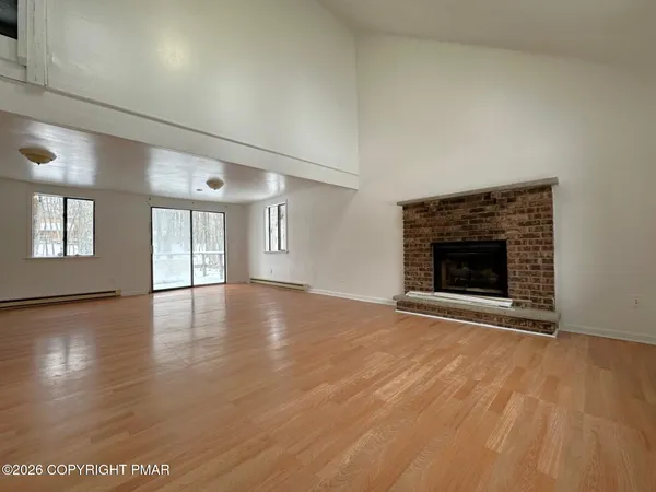an empty room with wooden floor fireplace and windows