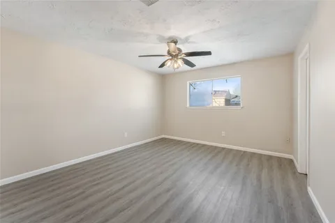 an empty room with wooden floor ceiling fan and window