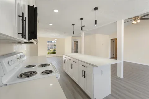 a kitchen with granite countertop a white stove top oven and white cabinets with wooden floor